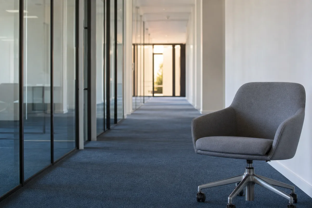 Couloir lumineux de bureaux avec cloisons vitrées et fauteuil vide au premier plan